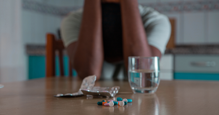 A person sitting at a table with pills and a glass of water