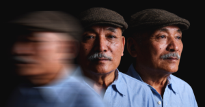 A person wearing a cap and blue shirt, with their image blurred and repeated to the left and right of the main subject against a dark background.