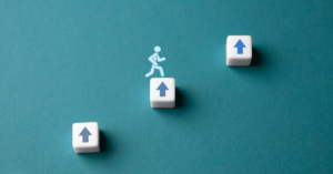 Three white cubes with blue arrows pointing up are arranged diagonally on a teal background, with a running figure icon jumping over the middle cube.