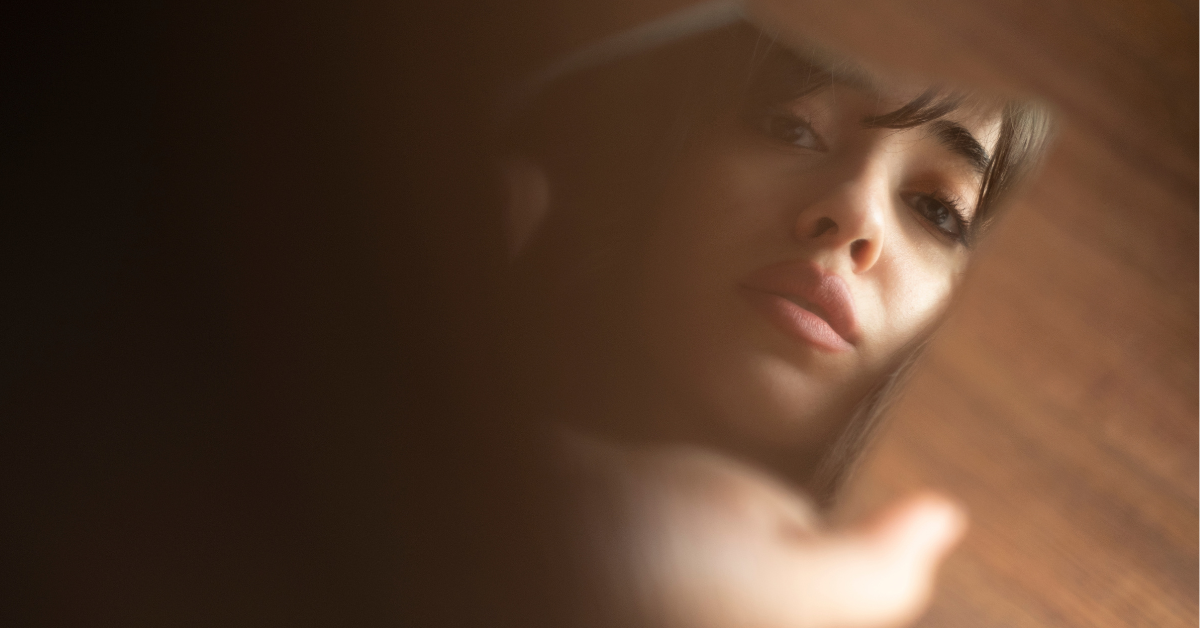 A close-up shot of a person looking into the camera, with shadows obscuring part of their face and body.
