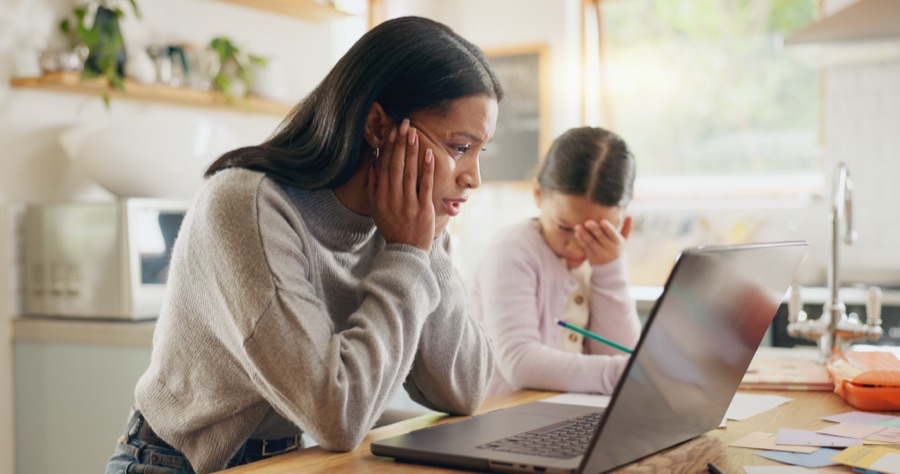 Woman looking stressed while working on a laptop with a child beside her