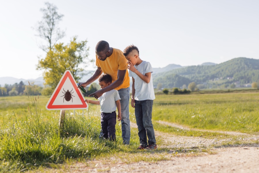 Father and two children examining a tick warning sign outdoors