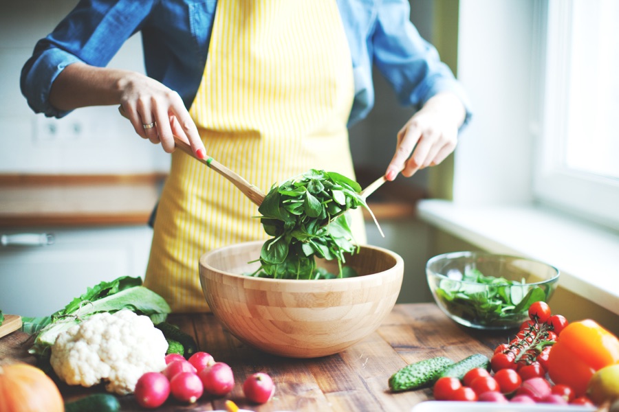 Person preparing a bowl of fresh vegetables in a kitchen