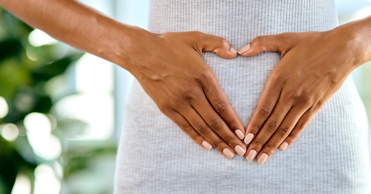 Hands forming a heart shape over a person's abdomen.