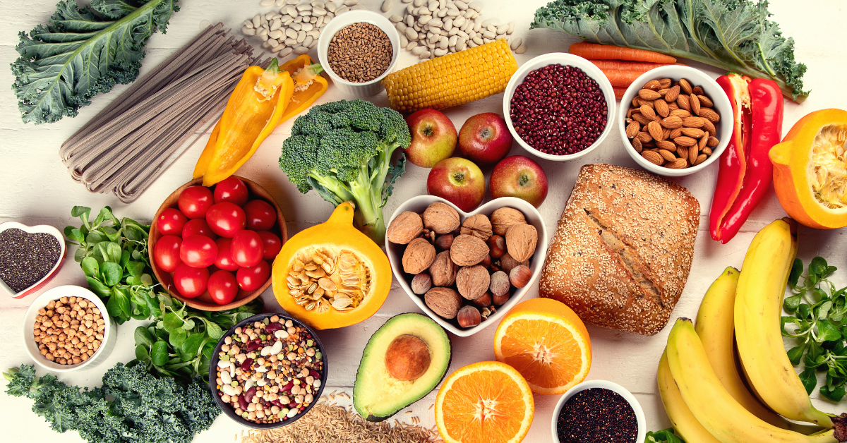 A spread of healthy foods including fruits, vegetables, nuts, seeds, grains, and bread.